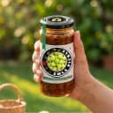 Hand holding Andhra Store Amla Pickle jar outdoors — authentic homemade pickle