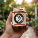 Hand holding Andhra Store Fish Pickle jar outdoors — authentic homemade pickle