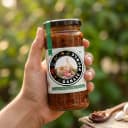 Hand holding Andhra Store Garlic Pickle jar outdoors — authentic homemade pickle
