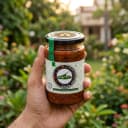 Hand holding Andhra Store Green Chilli Pickle jar outdoors — authentic homemade pickle