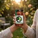 Hand holding Andhra Store Karela Pickle jar outdoors — authentic homemade pickle