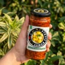 Hand holding Andhra Store Lemon Pickle jar outdoors — authentic homemade pickle