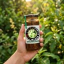 Hand holding Andhra Store Mango Pickle jar outdoors — authentic homemade pickle