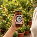 Hand holding Andhra Store Prawn Pickle jar outdoors — authentic homemade pickle