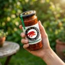 Hand holding Andhra Store Red Chilli Pickle jar outdoors — authentic homemade pickle