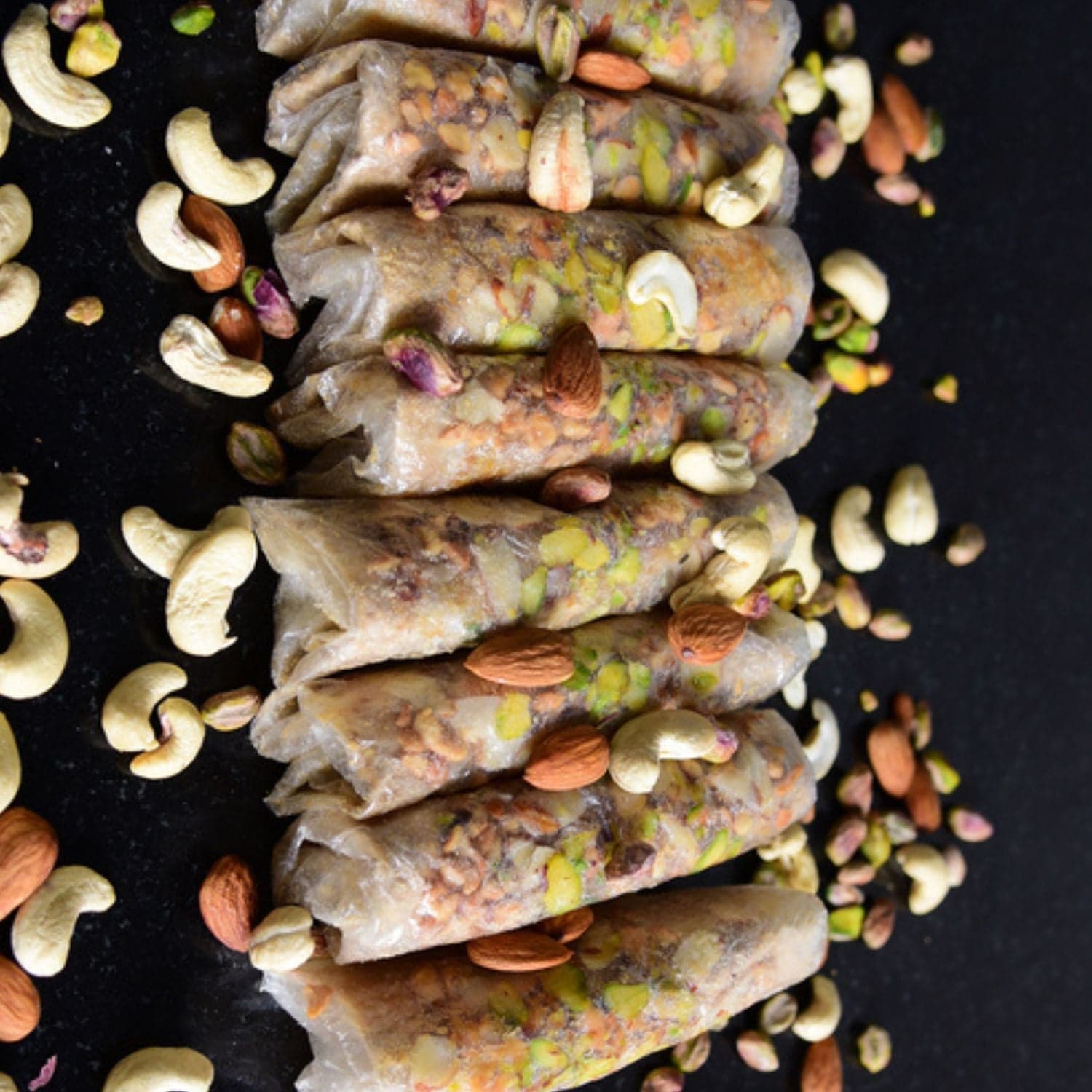 Pootharekulu — thin Andhra rice paper rolls with dry fruit filling, laid on dark surface